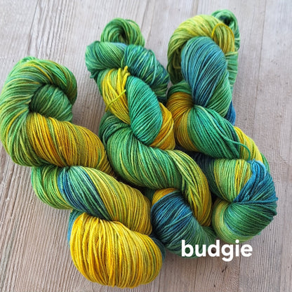 Green and yellow skeins of yarn on a wooden surface with 'budgie' label.
