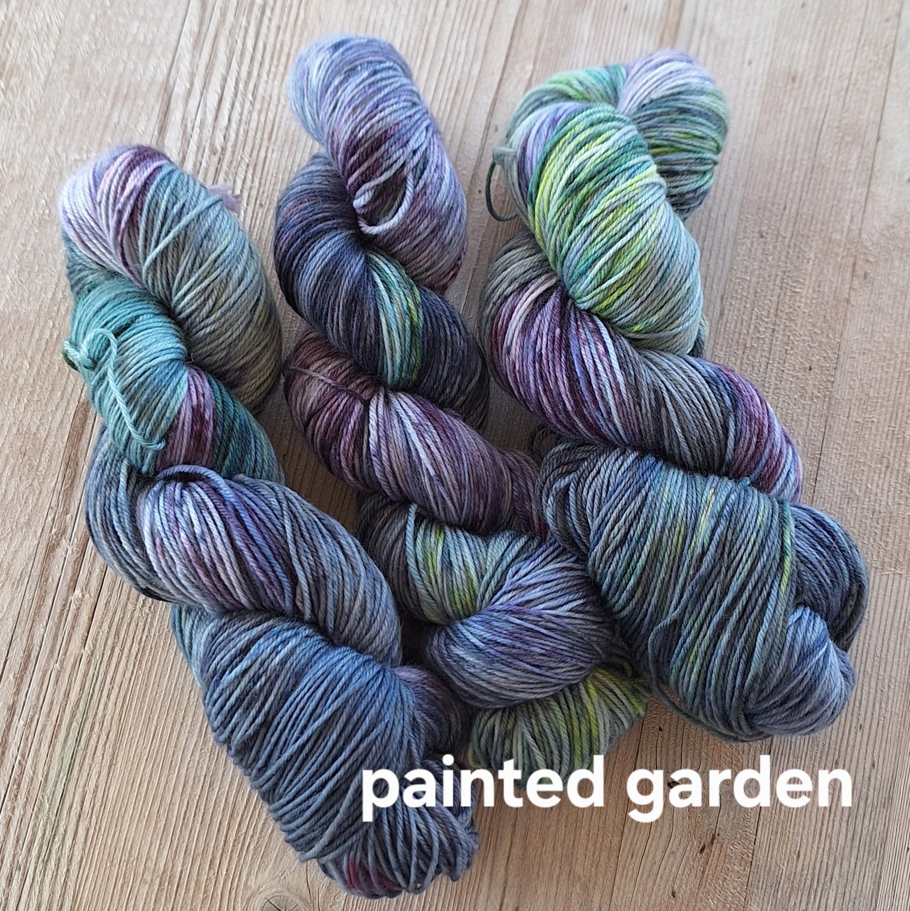 Multicolored yarn skeins on a wooden surface with 'Painted Garden' label.