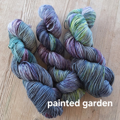 Multicolored yarn skeins on a wooden surface with 'Painted Garden' label.