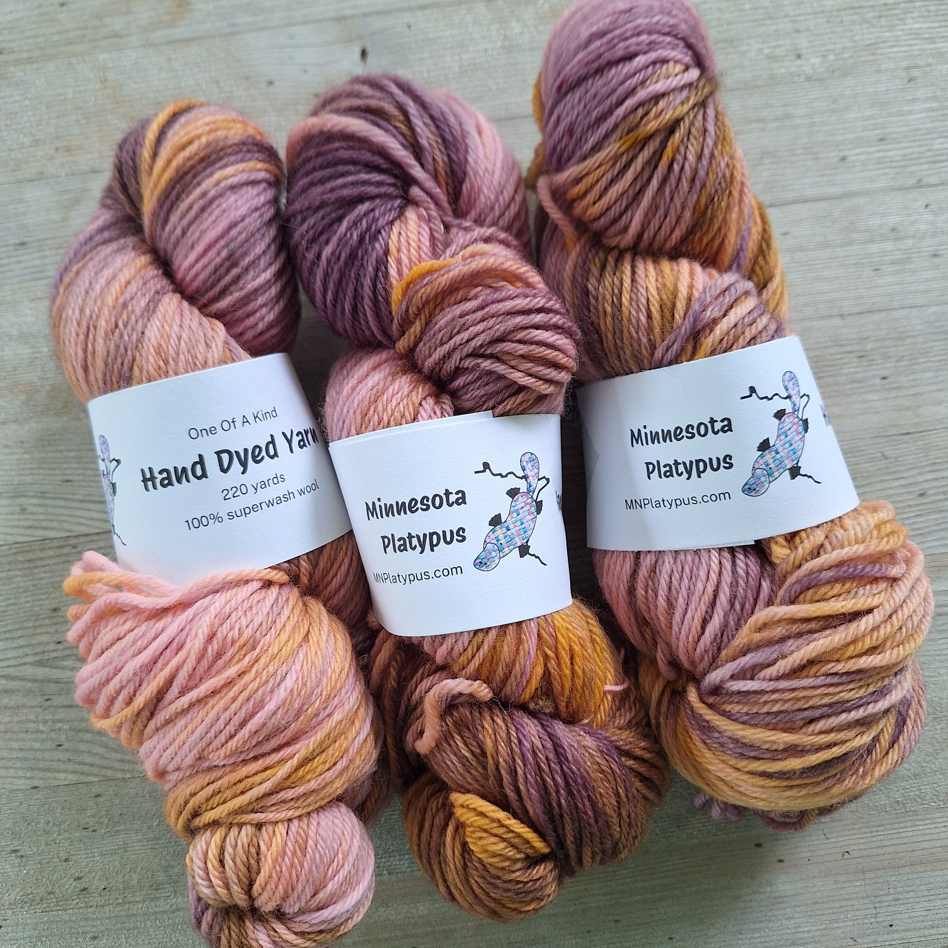 Three skeins of hand-dyed yarn with labels on a light wooden surface