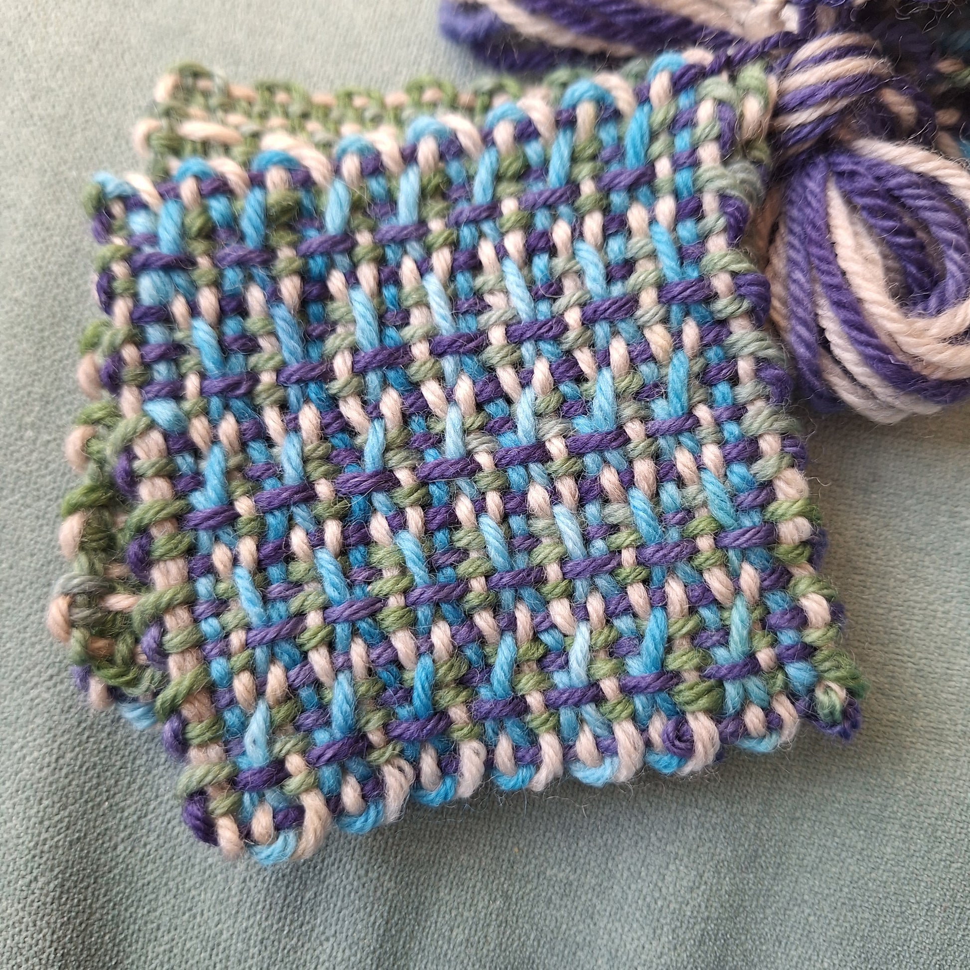 Hand-woven square using multicolored yarn on a light gray background