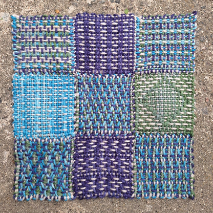 Woven fabric sample with blue, green, and purple patterns on a concrete surface